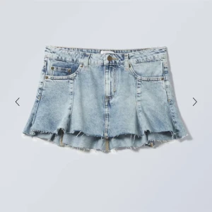 Blå kort jeanskjol från Weekday - Snygg blå jeanskjol från Weekday med rå kant. Kjolen har en kort längd och en lätt utsvängd form. Inga fickor baktill. Prislapp kvar
