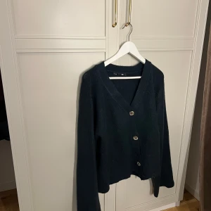 Svart kofta med knappar - Säljer en grön kofta med v-ringning och knappar framtill. Perfekt för kyligare dagar och enkel att matcha med olika outfits.