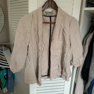 Beige bolero från H&M - Säljer en stilren beige bolero från H&M. Jackan har en öppen design utan knappar eller dragkedja och trekvartsärmar. Perfekt för en avslappnad look.