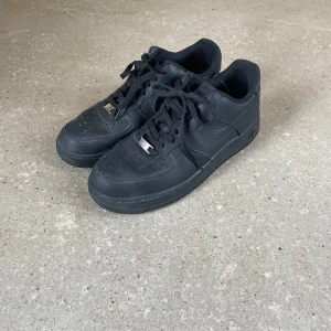 Svarta Nike Air Force sneakers - Snygga svarta Nike Air Force sneakers med klassisk design och snörning. Perfekta för en stilren look. Skorna har en robust sula och är tillverkade i syntetmaterial.