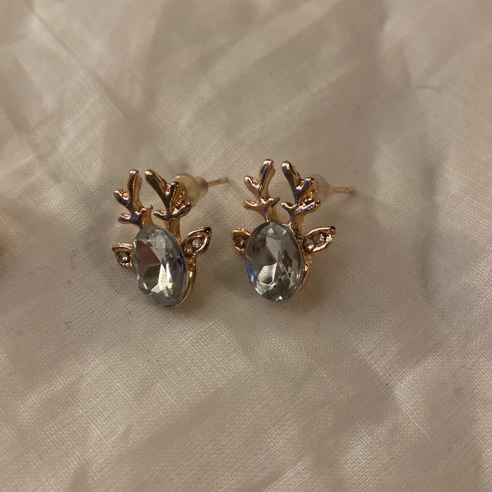 Säljer två par örhängen med renhornsdesign. Ett par har röda stenar och guldfärgade detaljer, medan det andra paret har klara stenar med silverfärgade detaljer. Perfekta för att ge en festlig touch till din outfit!. Asusteet.