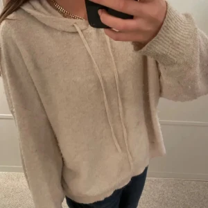 Beige stickad hoodie - Mysig beige stickad hoodie med långa ärmar och justerbar dragsko i huvan. Perfekt för kyliga dagar och ger en avslappnad stil. Passar bra till jeans eller leggings.