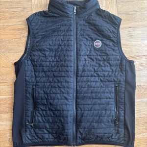 Svart quiltad väst från Colmar - Snygg svart quiltad väst från Colmar med dragkedja framtill. Perfekt för lager-på-lager under kyligare dagar. Västen har en stilren design med ett litet Colmar-märke på bröstet.