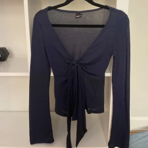 Mörkblå knyt tröja från Gina Tricot - Säljer en elegant mörkblå tröja från Gina Tricot. Tröjan har en v-ringad design med knytning framtill och långa ärmar. Perfekt för en stilren look.