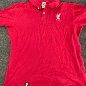 Röd pikétröja från L.F.C. - Säljer en snygg röd pikétröja från L.F.C. med broderad logga på bröstet. Tröjan har en klassisk krage med knappar och är perfekt för alla fotbollsfans. Passar bra till både vardag och matchdagar. Skicka ett meddelande vid intresse! ⚽️ Storlek L men passar M ochså. 