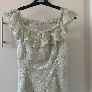 Ljusblå topp med volangdetaljer - Säljer en romantisk ljus klänning med vackra spetsdetaljer och volanger. Topp har en offshoulder-design som ger en elegant touch. Perfekt för speciella tillfällen! Passar som xs