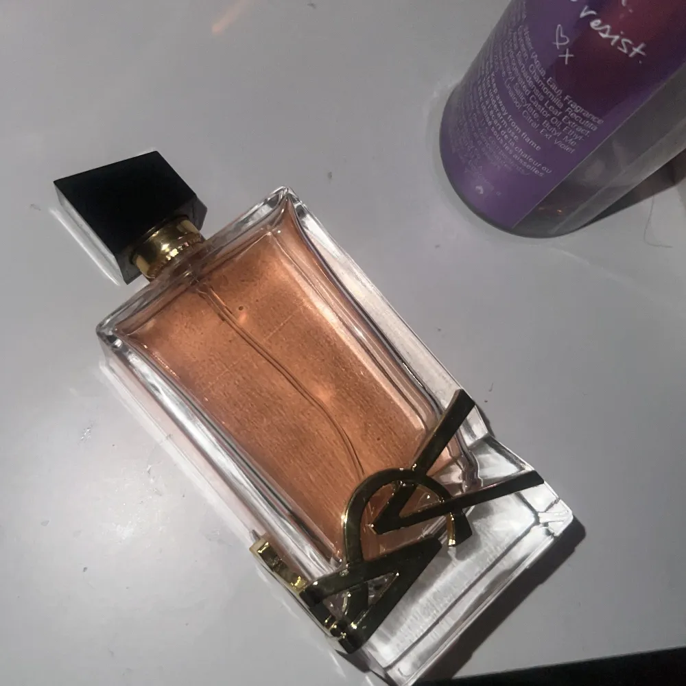 Elegant parfymflaska från Yves Saint Laurent med en stilren design. Flaskan är rektangulär med en svart kork och har en gyllene YSL-logga på framsidan. Innehållet har en varm, bärnstensfärgad ton som ger en lyxig känsla.. Perfume.