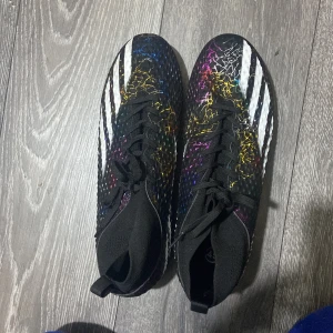 Färgglada fotbollsskor från Adidas - Snygga fotbollsskor från Adidas med ett unikt färgglatt mönster och vita detaljer. Skorna har snörning och dobbar för optimalt grepp på planen. Perfekta för den som vill sticka ut på fotbollsplanen.