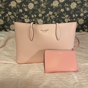 Rosa axelväska från Kate Spade - Säljer en stilren rosa axelväska från Kate Spade. Väskan har en enkel design med två handtag och en matchande liten plånbok. Perfekt för att bära dina dagliga nödvändigheter med stil. 💖nypris 2700 kr.