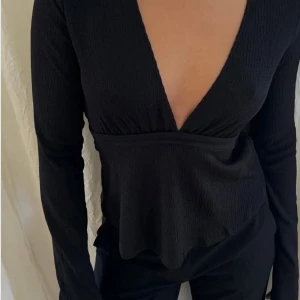 Svart V ringad topp med knytning - Snygg svart ribbad topp med djup v-ringning och knytband i midjan som är slutsålt, säljer då den bara använts en gång.