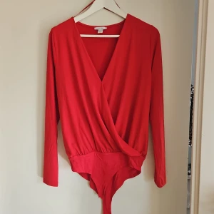 Röd omlott body - Snygg röd omlott body med långa ärmar och v-ringning. Perfekt för att skapa en stilren look. Tillverkad i ett mjukt och bekvämt material.