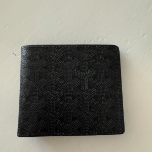 Svart plånbok  - Säljer en elegant svart plånbok från Go**rd med deras ikoniska mönster. Plånboken har flera kortfack och kommer i originalförpackning. Perfekt för den stilmedvetna som vill ha något exklusivt.