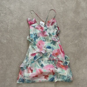 Blommig klänning från Zara - Säljer en superfin blommig klänning från Zara med volanger och tunna axelband. Klänningen har en härlig mix av rosa, blå och gröna toner. Den är även öppen i ryggen där banden korsar varandra,Perfekt för sommarens alla tillfällen! ❤️