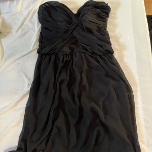 Svart axelbandslös klänning - Snygg svart axelbandslös klänning med draperad överdel och smickrande passform. Dragkedja i ryggen. Står storlek L men passar som en 36/38
