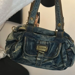 Jeansväska från Halfthesky - Cool jeansväska från Halfthesky med slitna detaljer och flera praktiska fickor. Väskan har robusta handtag och en snygg metallplatta framtill. ger y2k och 00s vibes! 