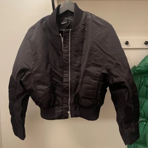 Svart bomberjacka från Gina Tricot - Snygg svart bomberjacka från Gina Tricot med dragkedja framtill. Jackan har en klassisk bomberstil med ribbad krage och indragen midja. Aldrig använd