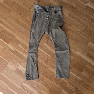 Beige byxor med knappar från humör - Snygga beige byxor med knappgylf och flera fickor. Perfekta för en avslappnad stil. Tillverkade i ett slitstarkt material som ger en bekväm passform.