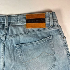 Ljusblå jeans från Jacob Cohen - Snygga ljusblå jeans från Jacob Cohen med en klassisk femficksdesign. De har en sliten look med revor på framsidan och en läderpatch baktill. Perfekt skick. Längd 34, midja 32