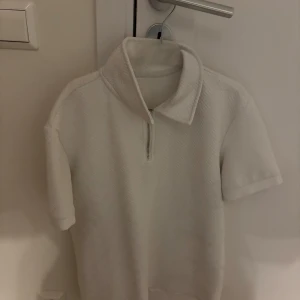 Vit kortärmad tröja med dragkedja - Säljer en stilren vit tröja med korta ärmar och dragkedja vid halsen. Perfekt för en avslappnad look.