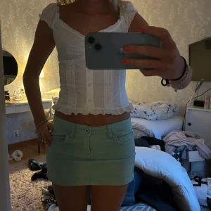 Mintgrön kortkjol - Snygg mintgrön kortkjol med en tight passform. Kjolen har en klassisk design med fickor och knappar framtill. Perfekt för en fräsch och somrig look!