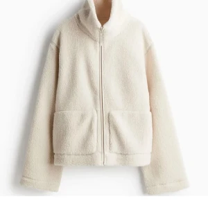 Vit teddyjacka från hm - Mysig vit teddyjacka med dragkedja och stora fickor framtill. Perfekt för kyliga dagar med sin fluffiga och varma design. Jackan har en hög krage och långa ärmar för extra komfort.