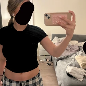 Svart kortärmad croppad topp - Säljer en stilren svart kortärmad croppad topp. Perfekt för en avslappnad look eller att matcha med högmidjade byxor. Toppen är enkel och mångsidig.