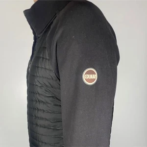 Svart jacka från Colmar - Snygg svart jacka från Colmar med quiltad design på framsidan och en diskret logga på ärmen. Jackan har en dragkedja framtill och långa ärmar, perfekt för kyligare dagar. En stilren och funktionell jacka för alla tillfällen.