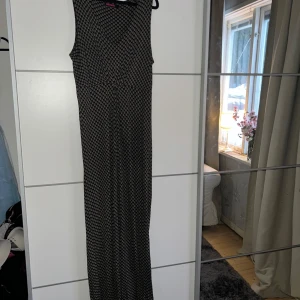 Mönstrad långklänning från Indiska - Säljer en snygg långklänning från Indiska med ett unikt mönster i svart och beige. Klänningen är ärmlös och perfekt för en stilren look. Passar utmärkt för både vardag och speciella tillfällen. Kontakta mig för mer info!