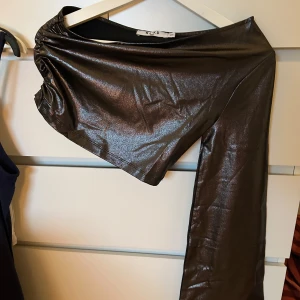 Glittrig oneshoulder topp från NA-KD - Snygg glittrig  oneshoulder topp från NA-KD. Perfekt för en kväll ute med sitt skimrande material och unika design. Toppen har en lång vid ärm och en snygg passform. Är i storlek XXS men passar XS med. Aldrig använd