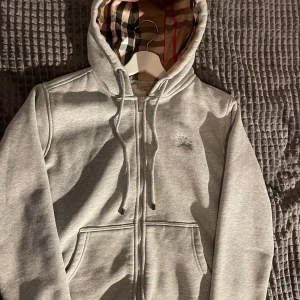 Grå kofta från Burberry - Säljer en stilren grå huvtröja från Burberry.jag säljer den på grund av att den tar plats i garderoben och inte änvänds längre(köpt här på plick) storlek S