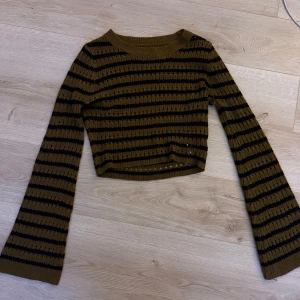 Randig stickad tröja - Säljer en fin randig stickad tröja i svart och brun. Tröjan är croppad med långa ärmar och har en avslappnad passform. Perfekt för en trendig look!