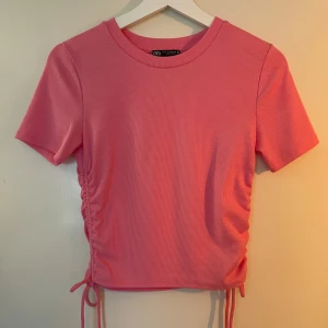 Rosa ribbad topp från Zara - Säljer en snygg rosa ribbad topp från Zara. Den har korta ärmar och knytning på sidorna för en justerbar passform. Använd gärna köp nu🌸