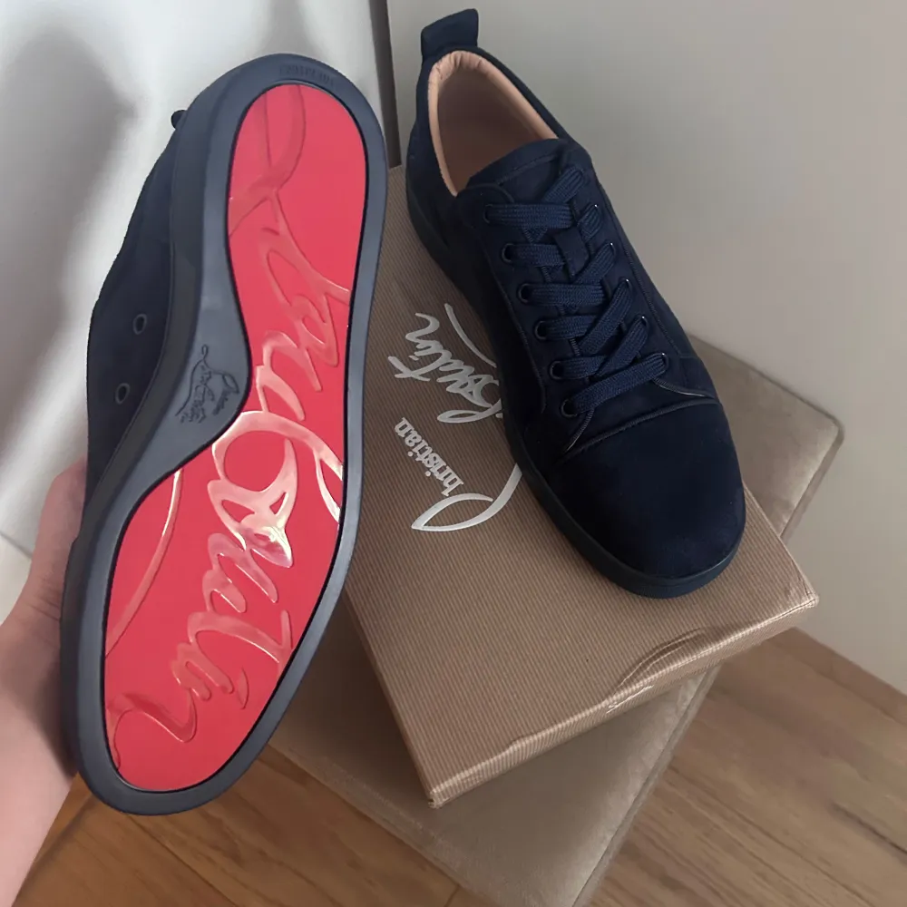 Snygga mörkblå sneakers från Christian Louboutin med den ikoniska röda sulan. Skorna har snörning och är tillverkade i mocka, vilket ger en lyxig känsla. Perfekta för att ge din outfit en exklusiv touch.. Kengät.