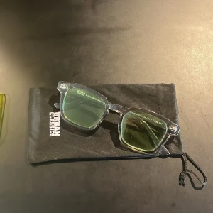 Solglasögon från Urban Classics - Snygga solglasögon från Urban Classics med transparent båge och gröna glas. Perfekta för en cool look. Kommer med ett svart fodral och ett neonfärgat etui för extra skydd.