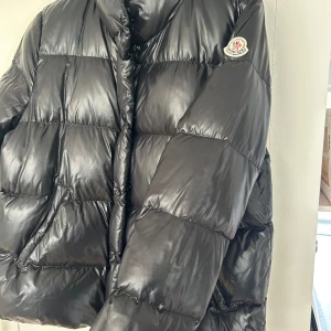 Svart dunjacka från Moncler - Säljer en snygg svart dunjacka från Moncler. Jackan har en glansig finish och är i väldigt bra skick med inga större slitningar. I storlek 5 men skulle säga passar M/ liten L. Den är äkta (om intresserad kan jag skicka äkthetsbevis). Inga kvitto medföljer. Modellen heter: Brethil Giubotto 