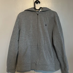 Grå hoodie från Polo  - Säljer en klassisk grå hoodie från Polo  med dragkedja och huva. Den har polo märket på högra bröstet och praktiska fickor framtill. Perfekt för en avslappnad stil. Den är i storlek.   xs/s den passar xs och s. Priset är inte satt öppen för alla förslag på pris 