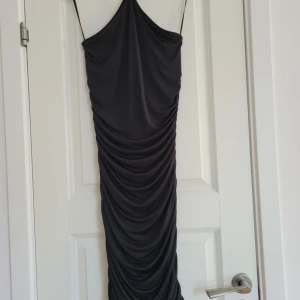 Svart klänning med rynkdetaljer - Snygg svart halterneck klänning och rynkdetaljer längs hela längden. Perfekt för en elegant kvällslook. Klänningen är gjort av töjbart tyg som ger en smickrande passform.