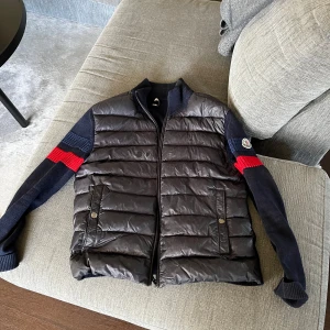 Tja säljer min moncler cardigan då den börjar bli för liten den är i storlek M har lagat den för fått några hål i den kolla bild 2 därav priset.. kan fraktas mot fraktkostnad. - Snygg svart pufferjacka med dragkedja och stickade ärmar i mörkblått och rött. Jackan har ribbad krage och muddar, samt två fickor framtill. Perfekt för kyliga dagar!