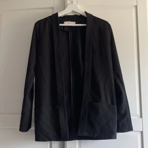 Svart kavaj från Pieces - Snygg svart kavaj från Pieces med en stilren design. Kavajen har långa ärmar och en öppen front utan knappar eller dragkedja. Perfekt för en elegant och minimalistisk look.