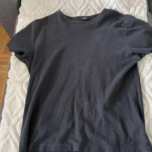 Svart t-shirt från H&M - Säljer en klassisk svart t-shirt från H&M i storlek M. T-shirten har en normal passform och är tillverkad i ett lite luftigare material. Tyvärr har den ett lite hål på sidan av tröjan.