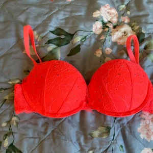  Superpush up från hm,neonkorallfärgad - Säljer en snygg bh med spets och strassdetaljer.Ger mycket push för bysten.Är väldigt liten i storleken så 70 b stämmer inte,är en 70 a tycker jag.Har lite små fläckar, se bilder.Den har justerbara axelband och en liten rosett framtill.Har köpt på Hm för många år sedan och är nu för liten.