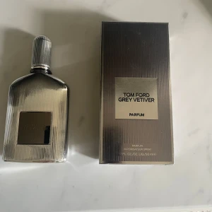 Tom Ford Grey Vetiver Parfum - Elegant och sofistikerad parfym från Tom Ford, Grey Vetiver, i en stilren silverfärgad flaska med räfflad design. Flaskan rymmer 50 ml och kommer i en matchande förpackning. Perfekt för den som söker en tidlös och klassisk doft.