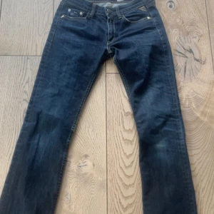 Mörkblå jeans från Replay - Snygga mörkblå jeans från Replay med broderad detalj på bakfickan. De har en klassisk femficksdesign och är tillverkade i Italien. Perfekta för en stilren look.