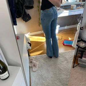 Blå bootcut jeans - Säljer ett par klassiska blå bootcut jeans med hög midja. De har en snygg passform som sitter bra över höfterna och går ut i en lätt utsvängning vid benen. Perfekta för en avslappnad stil.