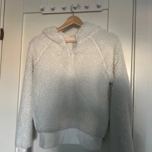 Vit fleece hoodie - Mysig vit hoodie i fleece med dragkedja framtill. Perfekt för kyliga dagar med sin fluffiga och varma design. Den har en huva och långa ärmar, vilket gör den extra bekväm och skyddande mot kylan.