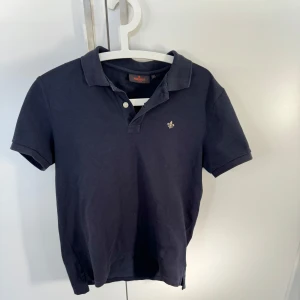 Mörkblå pikétröja från Morris - Snygg mörkblå pikétröja från Morris med klassisk krage och knappdetaljer. Perfekt för en stilren look. Liten broderad logga på bröstet ger en extra touch. Org pris 1000 kr