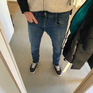 Blå jeans från Replay - Snygga blå jeans från Replay i modellen Anbass Hyperflex. De har en klassisk femficksdesign och en bekväm passform. Perfekta för en stilren look. Han på bilden är 186 och de sitter perfekt på han.