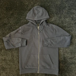 Mörkblå hoodie med dragkedja - Säljer en stilren mörkblå hoodie med dragkedja och justerbar huva. Tröjan har långa ärmar och praktiska fickor framtill. Perfekt för en avslappnad look.