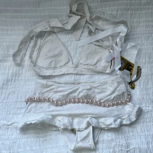 Vit bikini från Juicy Couture - NYTT skick med defekter (missfärgningar)! Vet ej om den är äkta eller inte. Snygg vit bikini från Juicy Couture med broderade blommor och volangdetaljer. Toppen har knytband och byxan pryds av pärlor och texten 'Juicy' i svart. Perfekt för sommarens stranddagar!