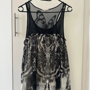 Svart och grå topp med fjärilsdetalj - Snygg svart och grå topp med ett unikt fjärilsmönster på ryggen. Toppen har ett transparent mesh-överdel och ett abstrakt mönster på kjolen. Perfekt för dig som vill sticka ut!